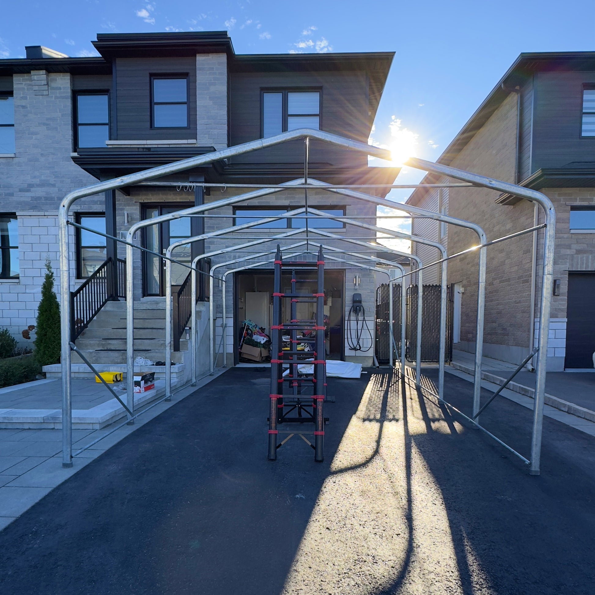 Metal carport structure in front of a residential house with sunlight casting shadows.