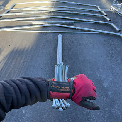 Hand wearing a glove holding nails with metal rods on a concrete surface