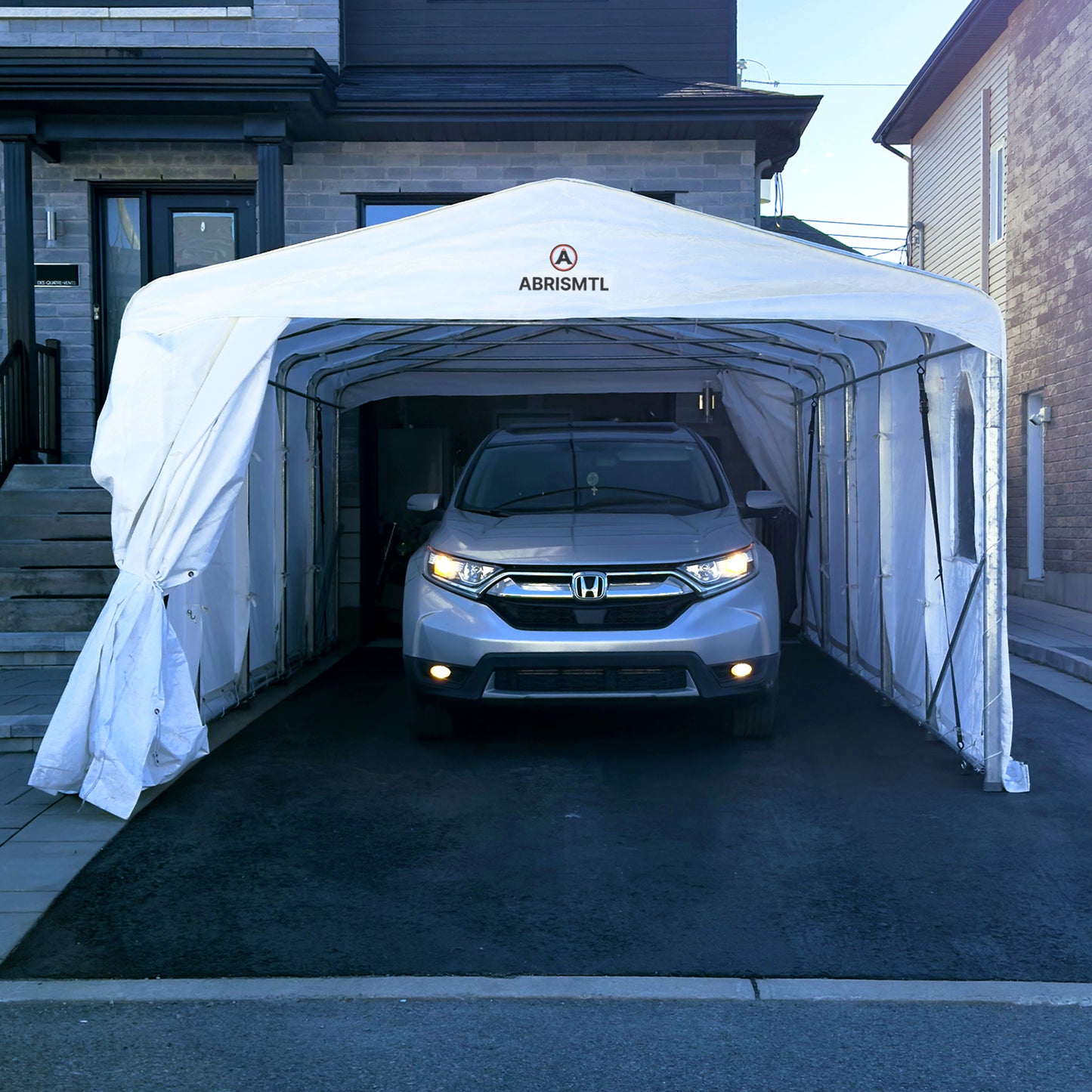 Car parked inside a white carport with 'ABRIS MTL' branding in front of a house.